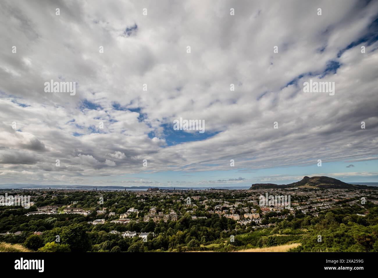 Von einem malerischen Hügel aus aufgenommen, fängt die weitläufige Aufnahme die vielfältigen Wandteppiche von Dublins Vierteln unter einem riesigen Himmel voller wehender Wolken ein. Stockfoto