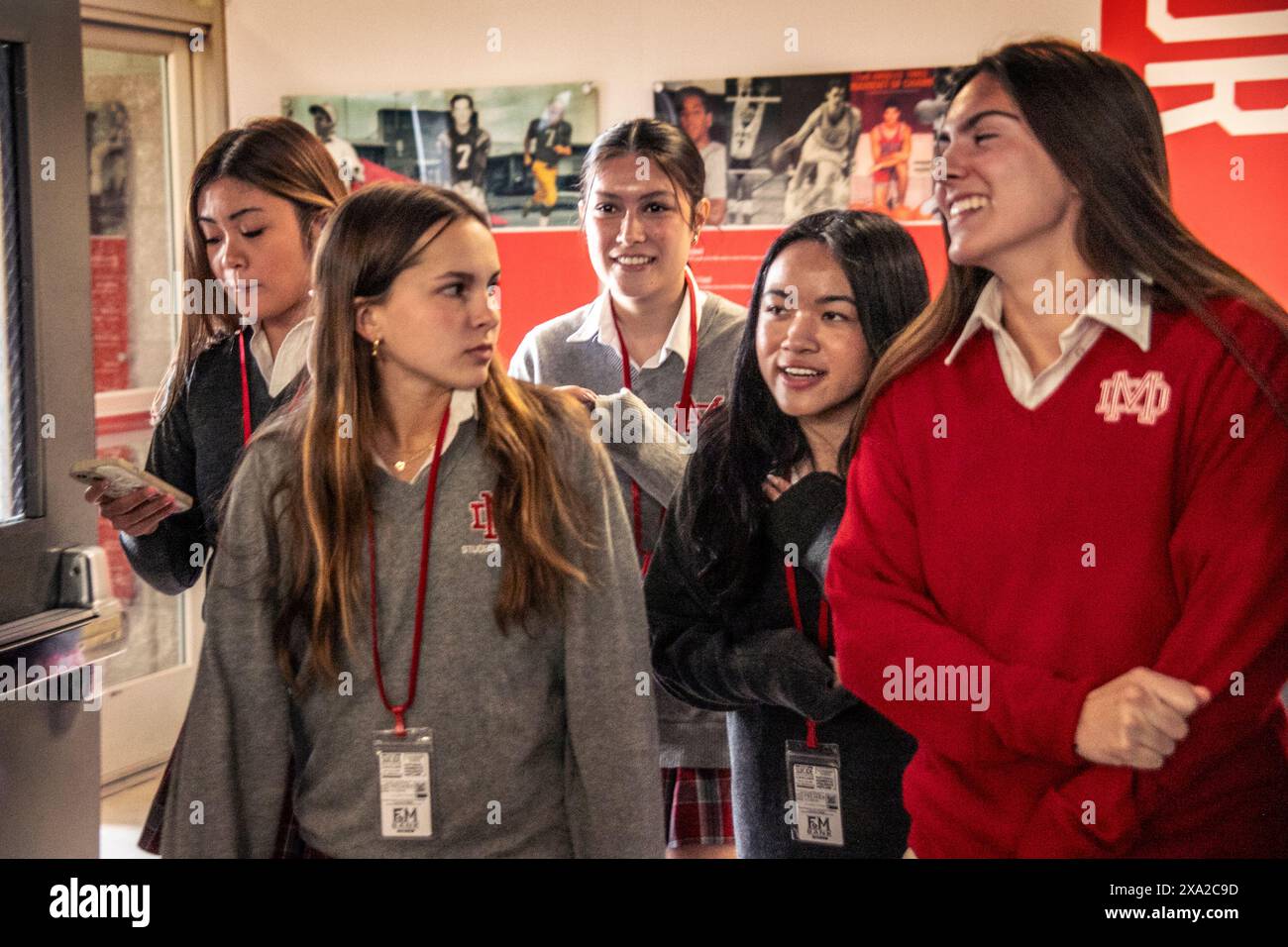 Uniformierte kaukasische und asiatische Teenager-Freundinnen an einer südkalifornischen katholischen High School interagieren im Schulflur. Stockfoto