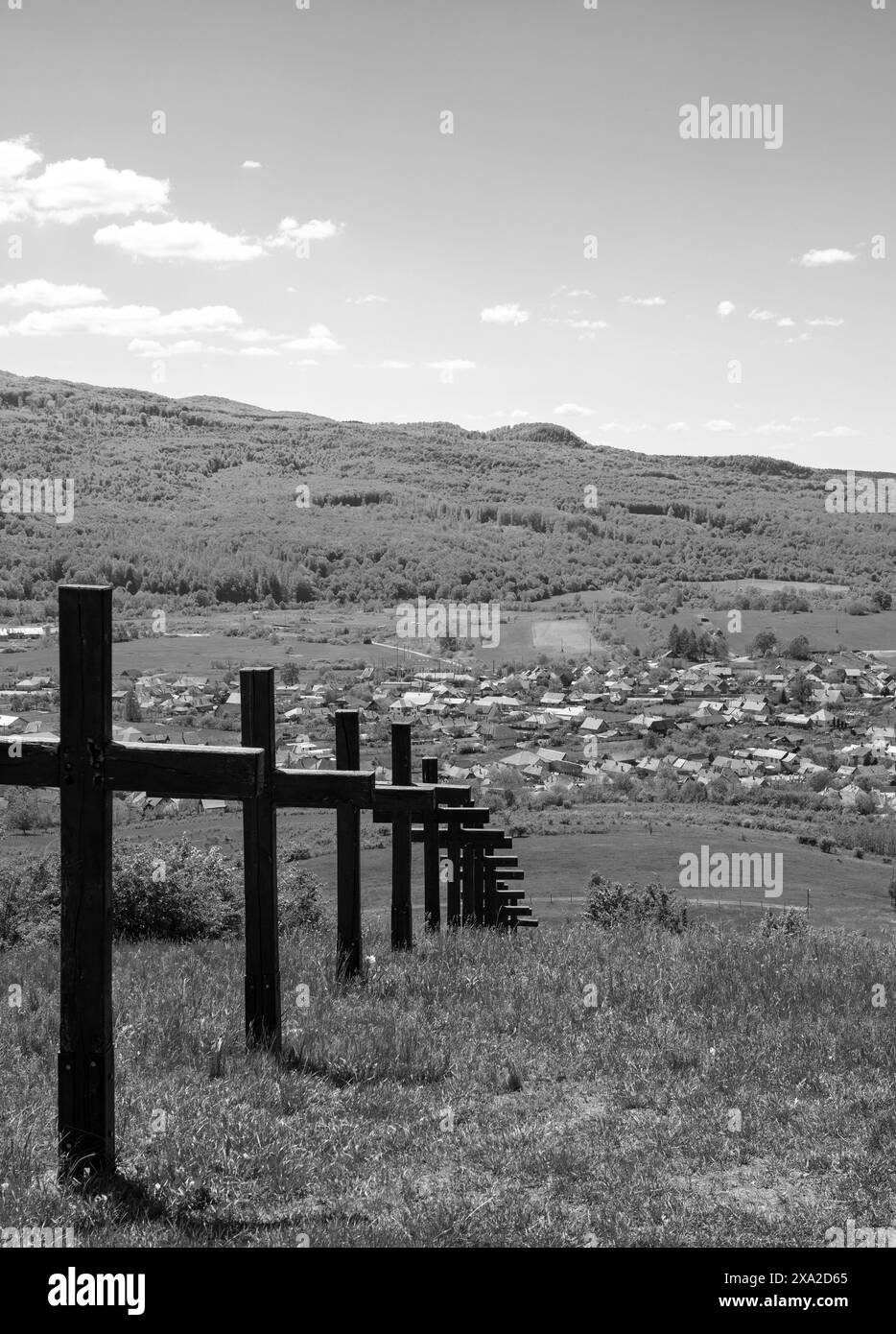 Ein monochromes Bild einer Reihe von Kreuzen auf einem Hügel mit Blick auf die Dorfhäuser. Stockfoto