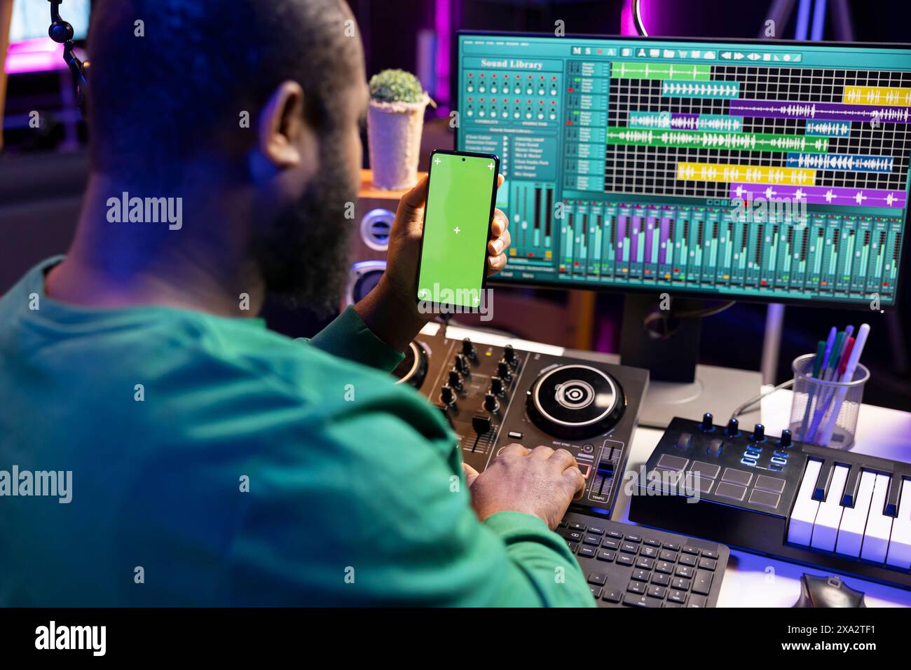 afroamerikanischer Audioingenieur, der Titel mit der daw-Software aufnimmt und bearbeitet, betrachtet die Greenscreen-Anzeige. Junger Komponist, Sänger, der Songs für seine neuen Lieder produziert, Heimstudio. Stockfoto