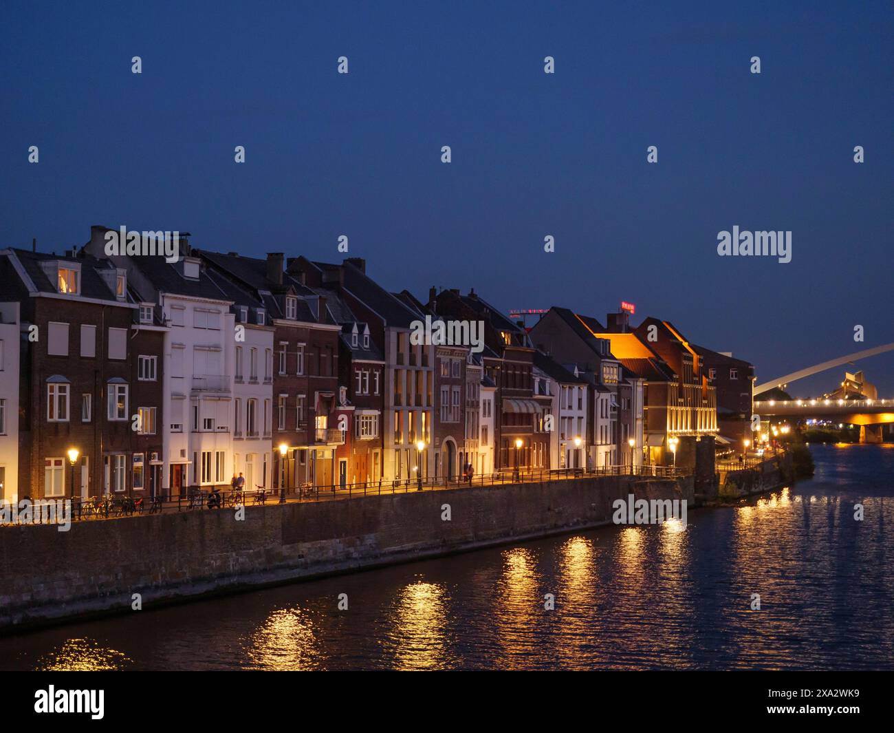 Stadthäuser entlang eines Flusses bei Nacht, beleuchtete Fenster im Wasser, ruhige Atmosphäre, Maastricht, Niederlande Stockfoto