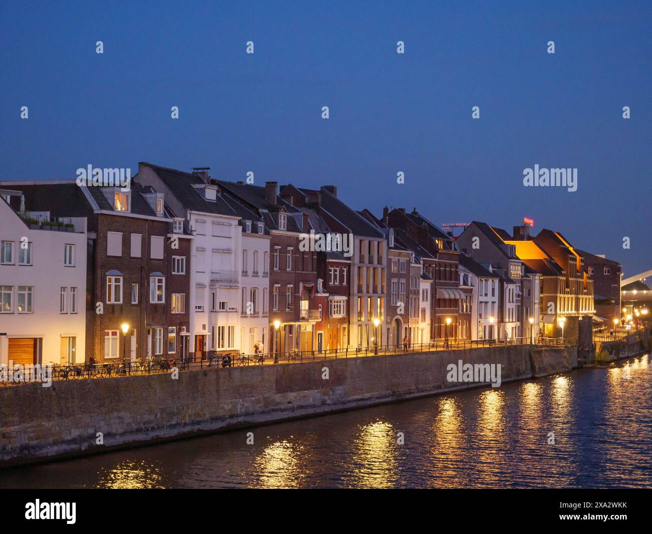 Stadthäuser entlang eines Flusses bei Nacht, beleuchtete Fenster im Wasser, ruhige Atmosphäre, Maastricht, Niederlande Stockfoto