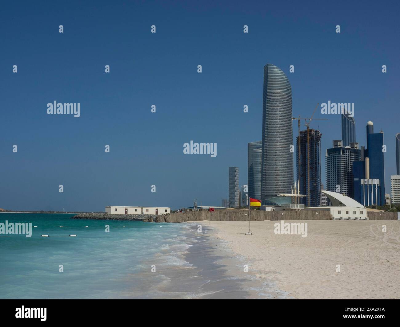 Küstenszene mit einem modernen Wolkenkratzer und benachbarten Gebäuden an einem Sandstrand unter klarem Himmel, Abu Dhabi, Vereinigte Arabische Emirate Stockfoto