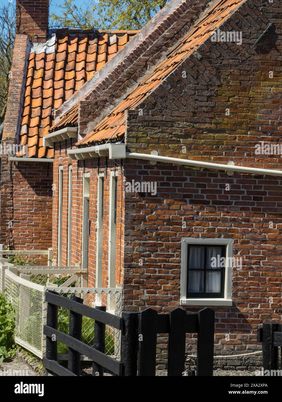 Traditionelle Backsteinhäuser mit Ziegeldächern und Zäunen leuchten in der Sonne, Enkhuizen, Nirderlande Stockfoto