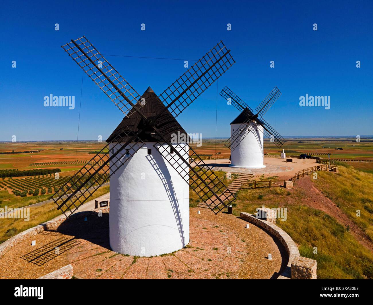 Zwei Windmühlen stehen auf einem sonnigen Hügel in einer weiten Feldlandschaft unter klarem Himmel, aus der Vogelperspektive: Alcazar de San Juan, Ciudad Real, Castilla-La Mancha Stockfoto