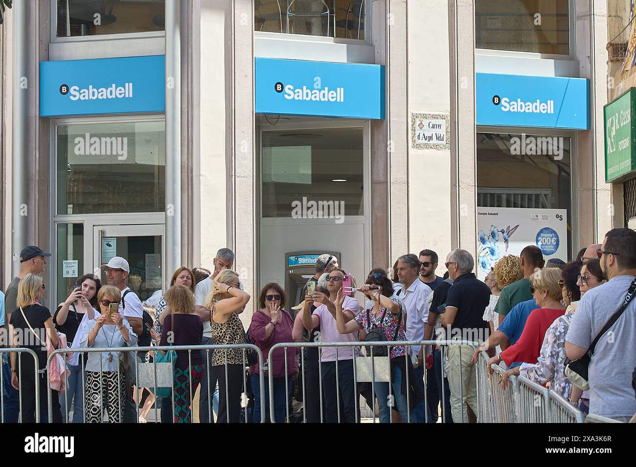 Sitges, Barcelona, Spanien-03. Juni 2024: Crowd beobachtet an einem sonnigen Tag eine Blumenausstellung auf der Straße der Banco Sabadell Niederlassung in Sitges. Stockfoto