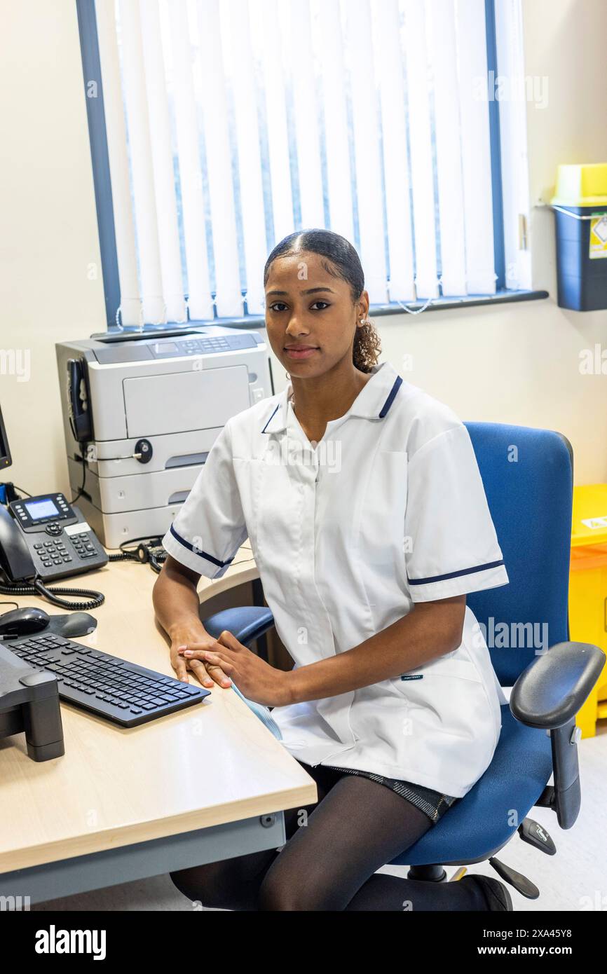 Krankenschwester sitzt an einem Schreibtisch mit einem Computer in einer Arztpraxis, Großbritannien Stockfoto