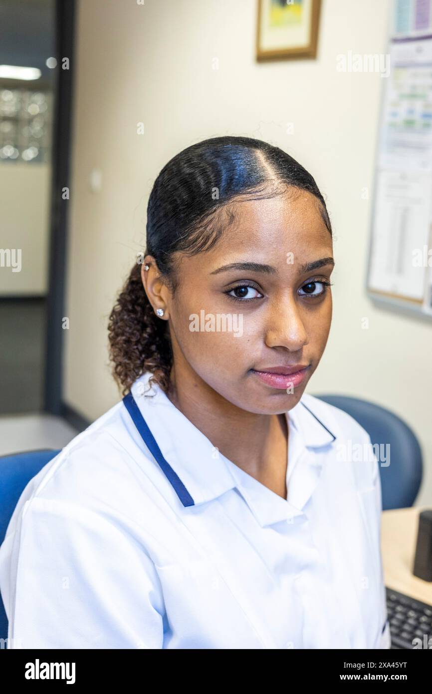 Krankenschwester sitzt an einem Schreibtisch mit einem Computer in einer Arztpraxis, Großbritannien Stockfoto