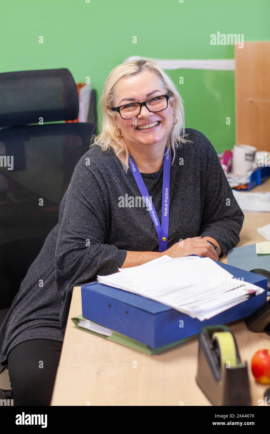 Lächelnde Frau, die in einer Arztpraxis mit Papieren und Bürobedarf am Schreibtisch sitzt Stockfoto