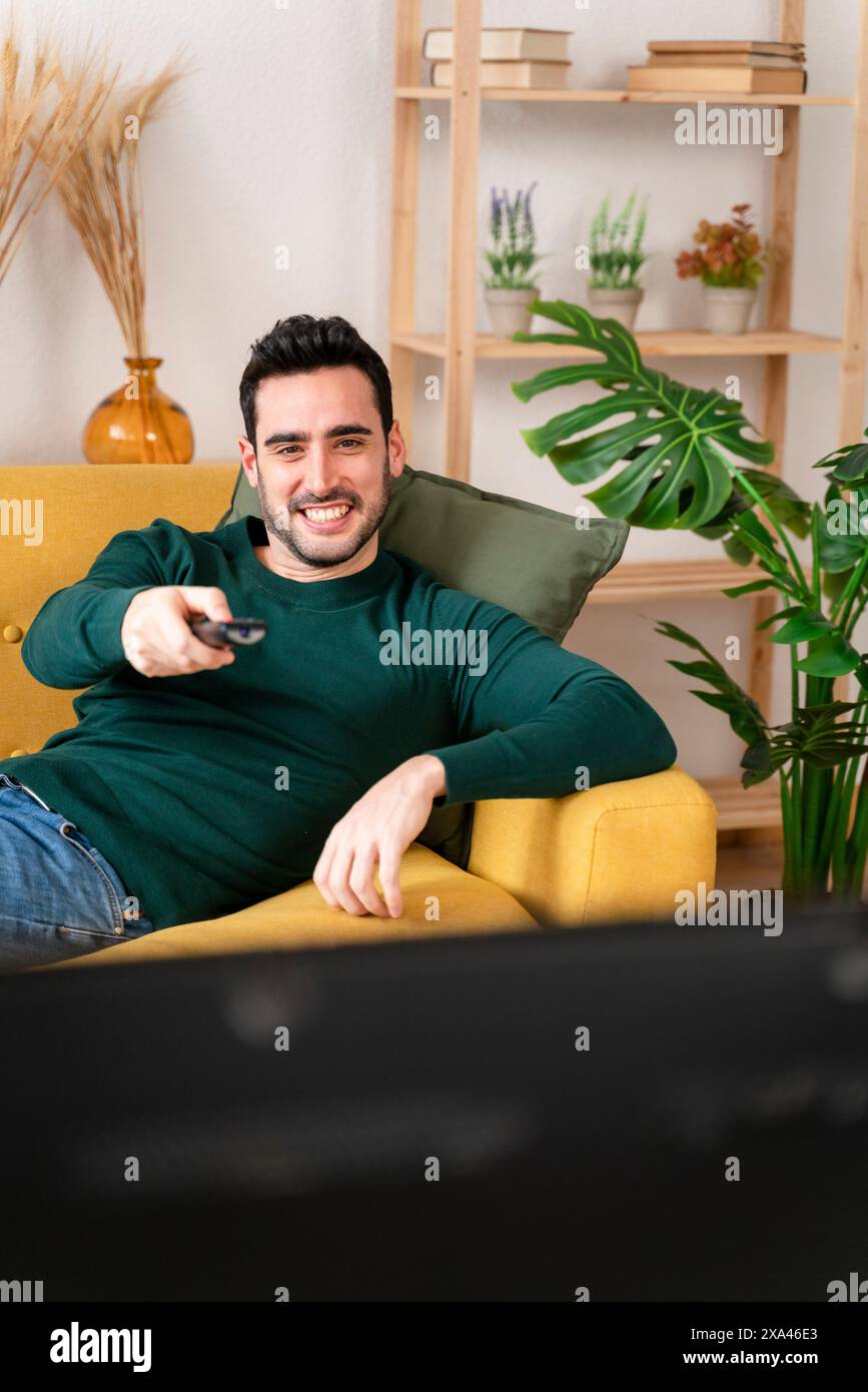 Mann, der sich auf einer Couch mit Fernbedienung in der Hand entspannt. Stockfoto