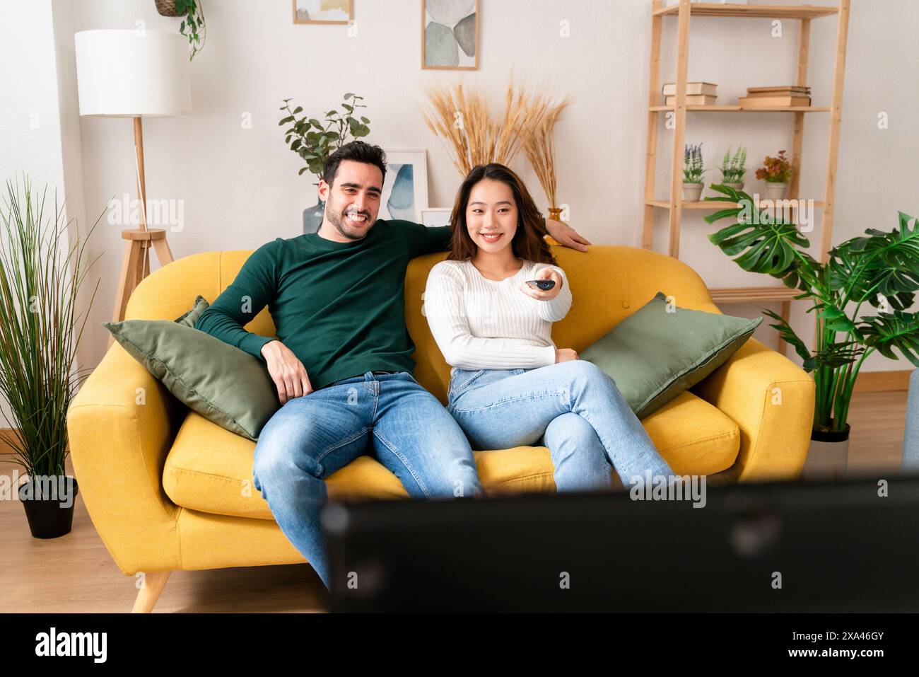 Paare entspannen auf einem gelben Sofa mit Fernbedienung Stockfoto