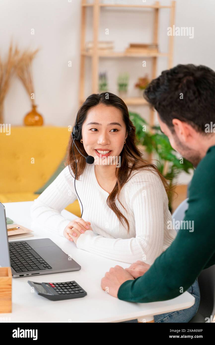 Eine junge Frau mit Headset am Schreibtisch, die mit einem Mann spricht Stockfoto