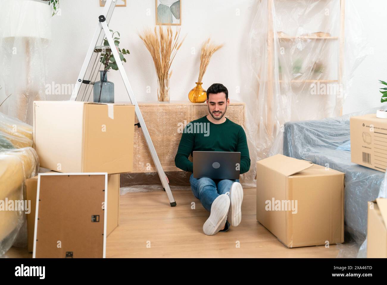 Mann mit Laptop, der auf dem Boden zwischen Umzugskästen sitzt. Stockfoto