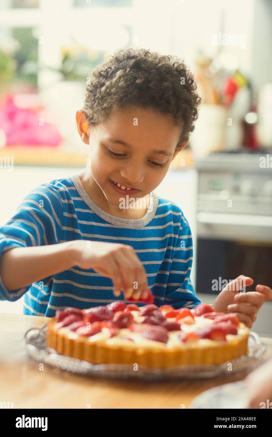 Junge, der Erdbeeren zum Kuchen hinzufügt Stockfoto