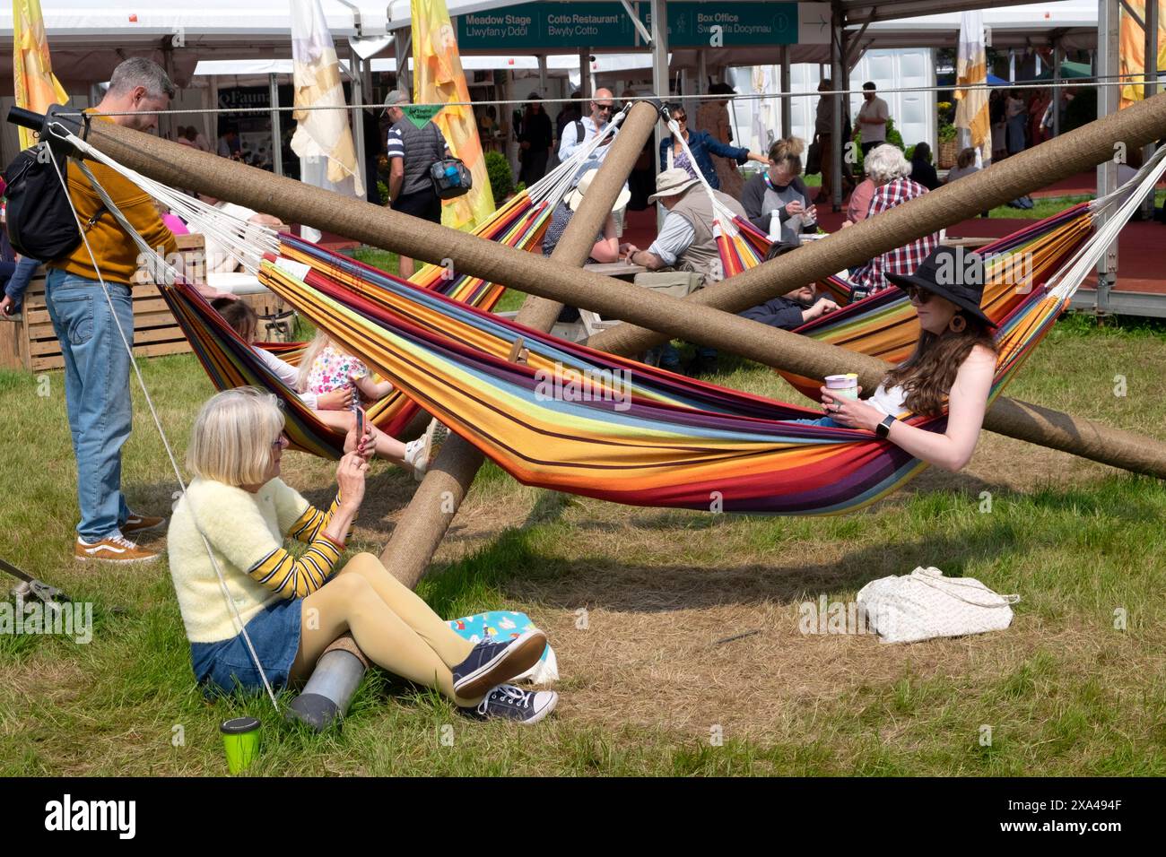 Frau mit Handy fotografiert Person sitzend in der Hängematte schwarze Sonnenhut Hay Festival 2024 Hay-on-Wye Wales Großbritannien Großbritannien KATHY DEWITT Stockfoto