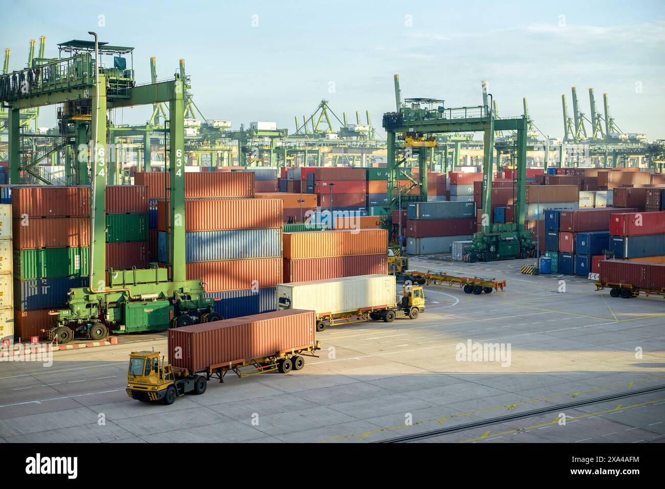 Ein belebtes Containerterminal mit Stapeln von mehrfarbigen Containern, Kränen im Hintergrund und automatisierten geführten Fahrzeugen, die Fracht transportieren. Stockfoto