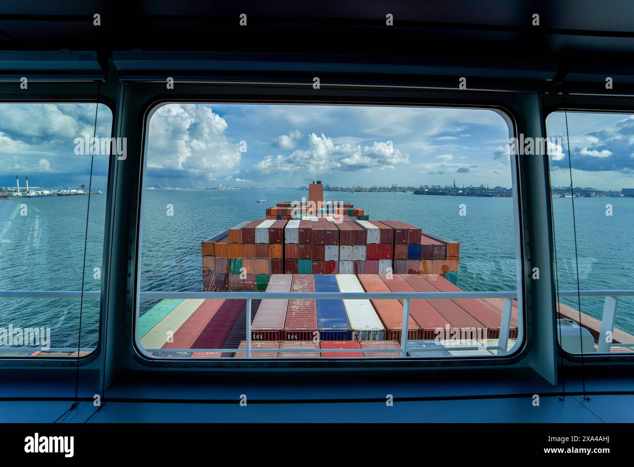Ein Blick vom Brückenfenster eines Schiffes mit Blick auf einen großen Stapel farbenfroher Schiffscontainer auf dem Deck des Schiffes, mit dem Ozean und dem bewölkten Himmel im Hintergrund. Stockfoto