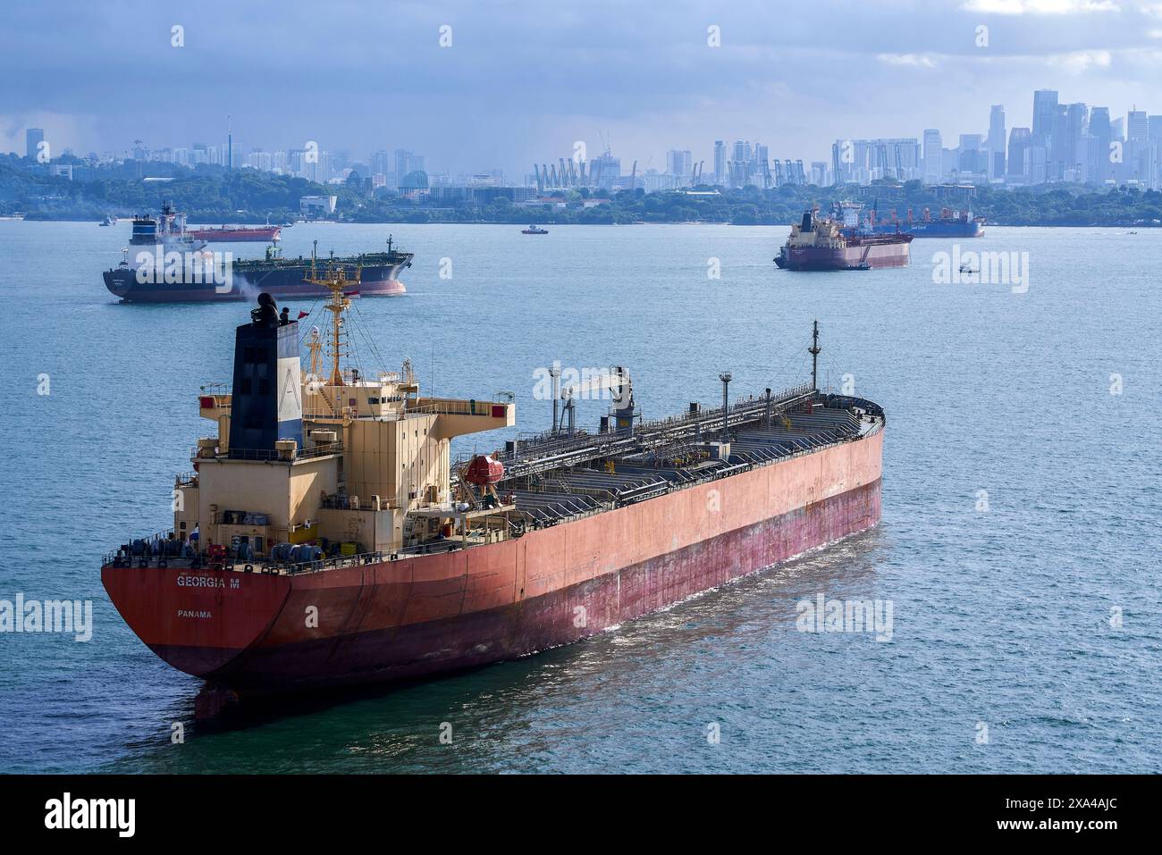 Ein großes Frachtschiff liegt auf dem Meer mit einer Skyline der Stadt im Hintergrund unter einem bewölkten Himmel vor Anker. Stockfoto
