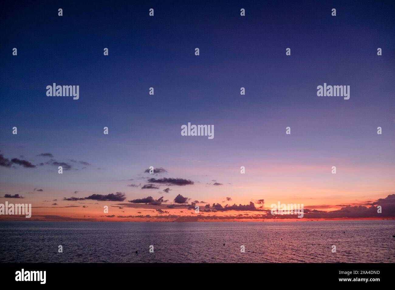 Eine ruhige Meereslandschaft bei Sonnenuntergang mit leuchtenden Orange- und Violetttönen, die den Himmel und sanfte Wellen auf der Wasseroberfläche bemalen. Stockfoto