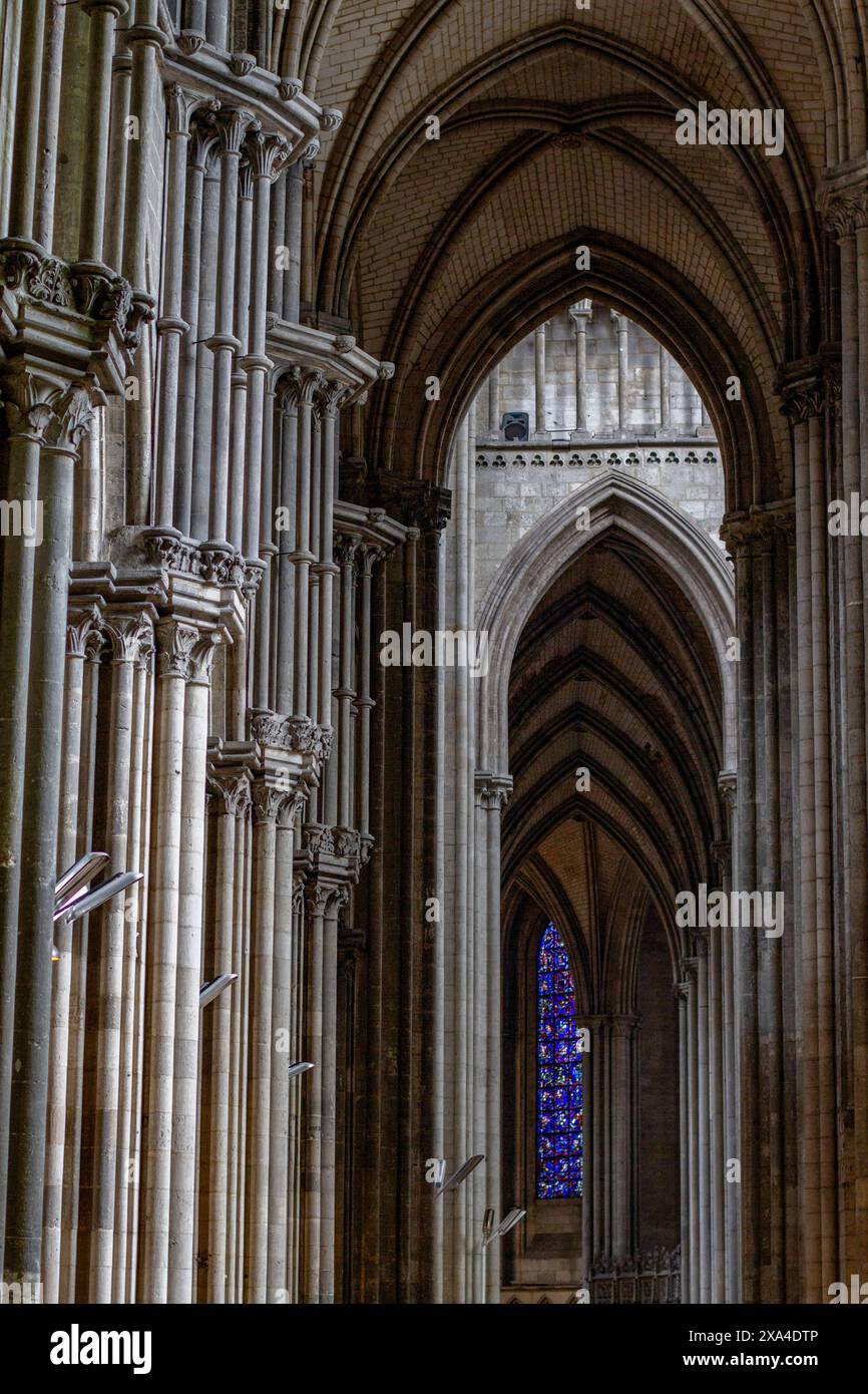 Das Bild zeigt das Innere einer gotischen Kathedrale mit hohen Bogendecken, Rippengewölben und verzierten Säulen, mit einem Buntglasfenster im Hintergrund. Stockfoto