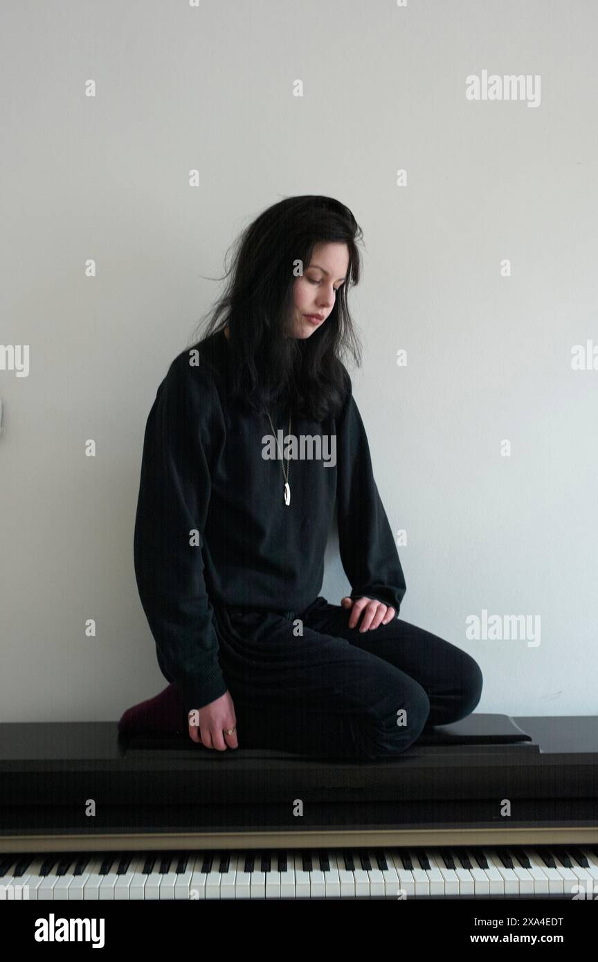 Ein junger Erwachsener sitzt im Kreuz auf einer Klavierbank mit geschlossenen Augen, scheint sich in einem friedlichen Zustand zu befinden. Stockfoto