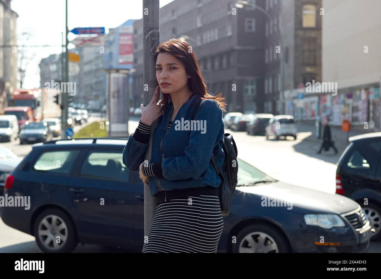 Eine Frau steht auf einem Bürgersteig der Stadt, hält ihr Handy ans Ohr, mit geparkten Autos und einer urbanen Straßenlandschaft im Hintergrund. Stockfoto