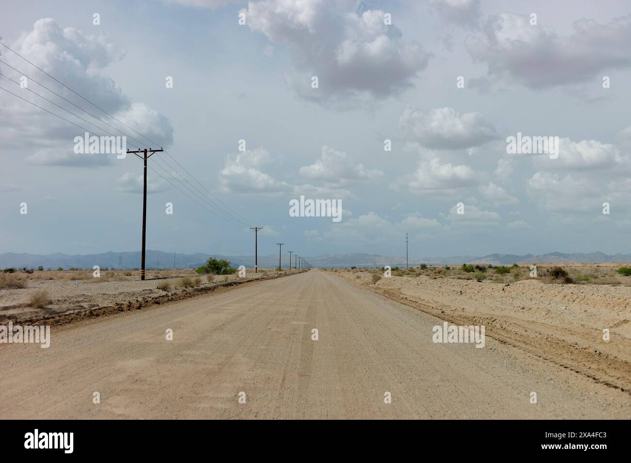 Eine verlassene Straße erstreckt sich bis in den Horizont unter bewölktem Himmel, flankiert von Telefonmasten und trockener Landschaft. Stockfoto