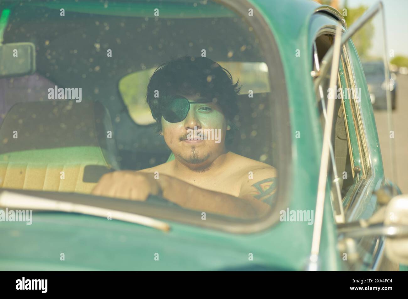 Ein Mann sitzt auf dem Fahrersitz eines grünen Oldtimers, trägt eine Sonnenbrille und blickt entspannt durch das offene Fenster. Stockfoto