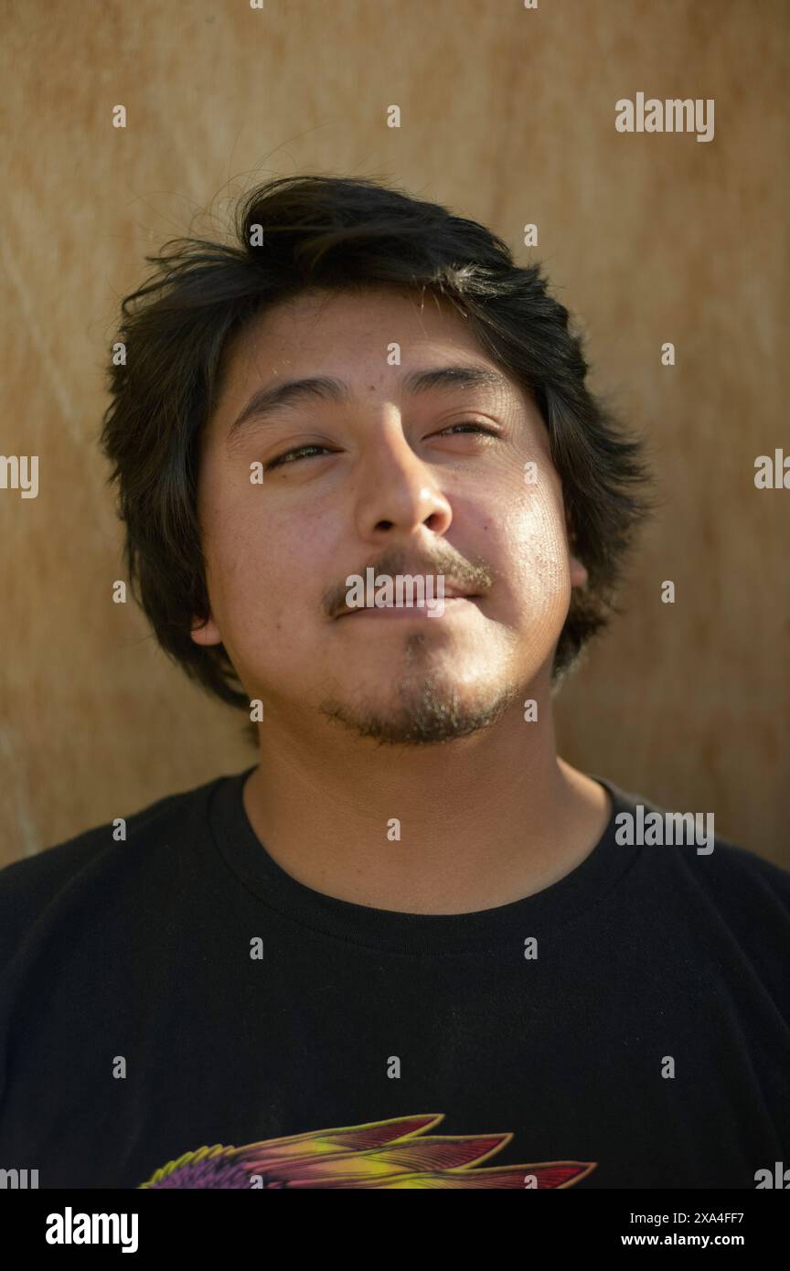 Ein Mann mit dunklem Haar und Schnurrbart steht vor einem beigen Hintergrund und blickt leicht nach oben mit einem ruhigen Gesichtsausdruck. Stockfoto