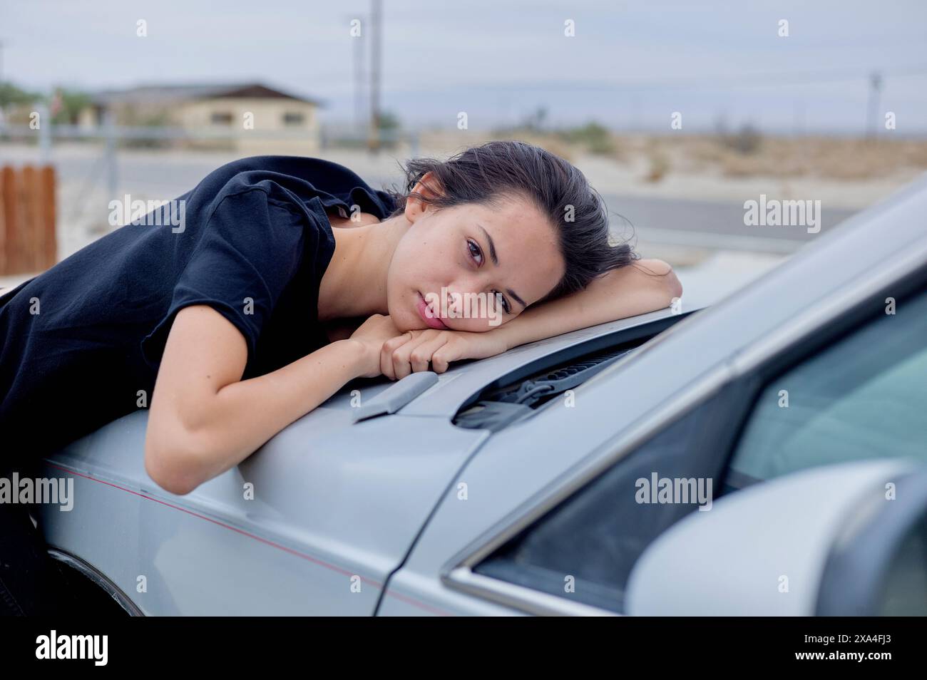 Eine Frau legt ihren Kopf auf ihre Hände, lehnt sich mit einem etwas kontemplativen Ausdruck auf die Seite eines Autos. Stockfoto