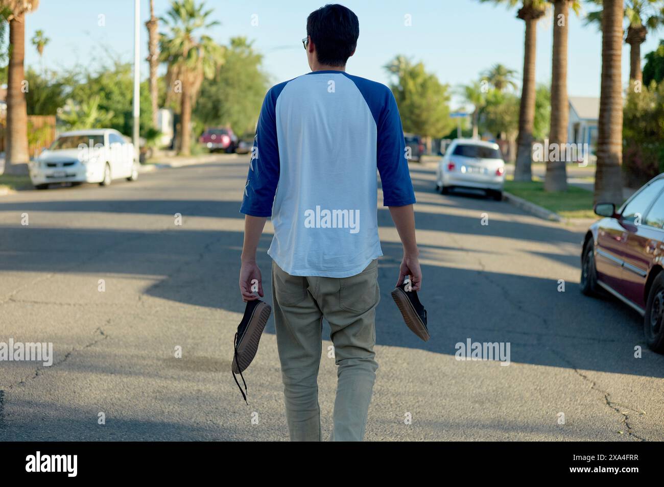 Ein Mann läuft eine Wohnstraße mit Sandalen in der Hand entlang, die an einem sonnigen Tag von hinten gefangen wurden. Stockfoto