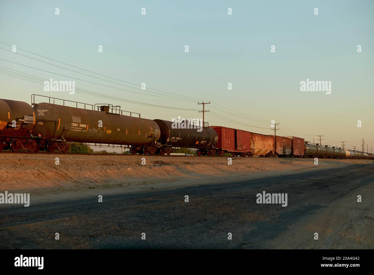 Ein Güterzug, bestehend aus verschiedenen Tank- und Boxwaggons, steht während einer ruhigen Dämmerung auf den Gleisen, mit einem klaren Himmel darüber. Stockfoto
