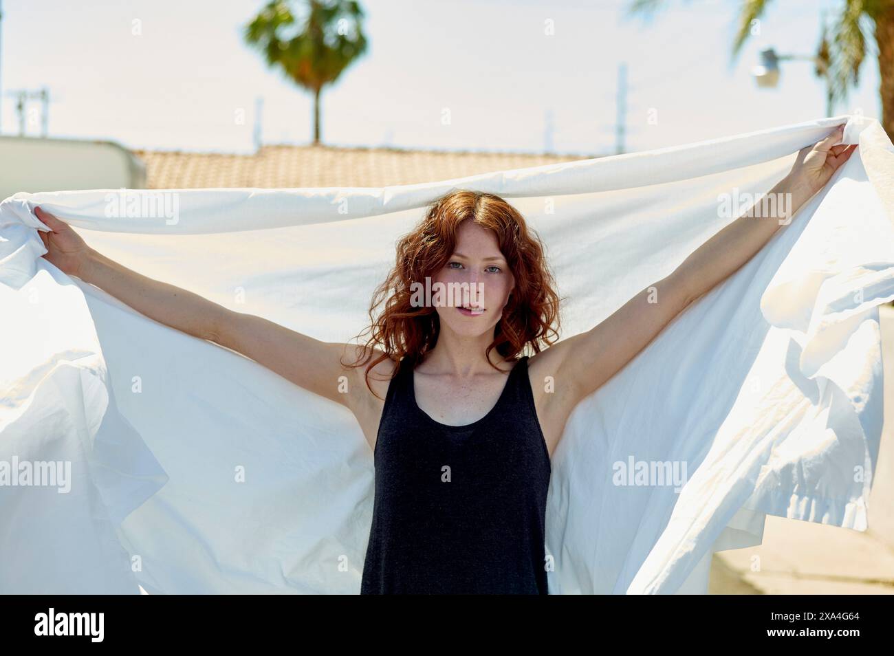 Eine Frau mit rotem Haar hält hinter sich ein weißes Tuch unter einem klaren blauen Himmel. Stockfoto