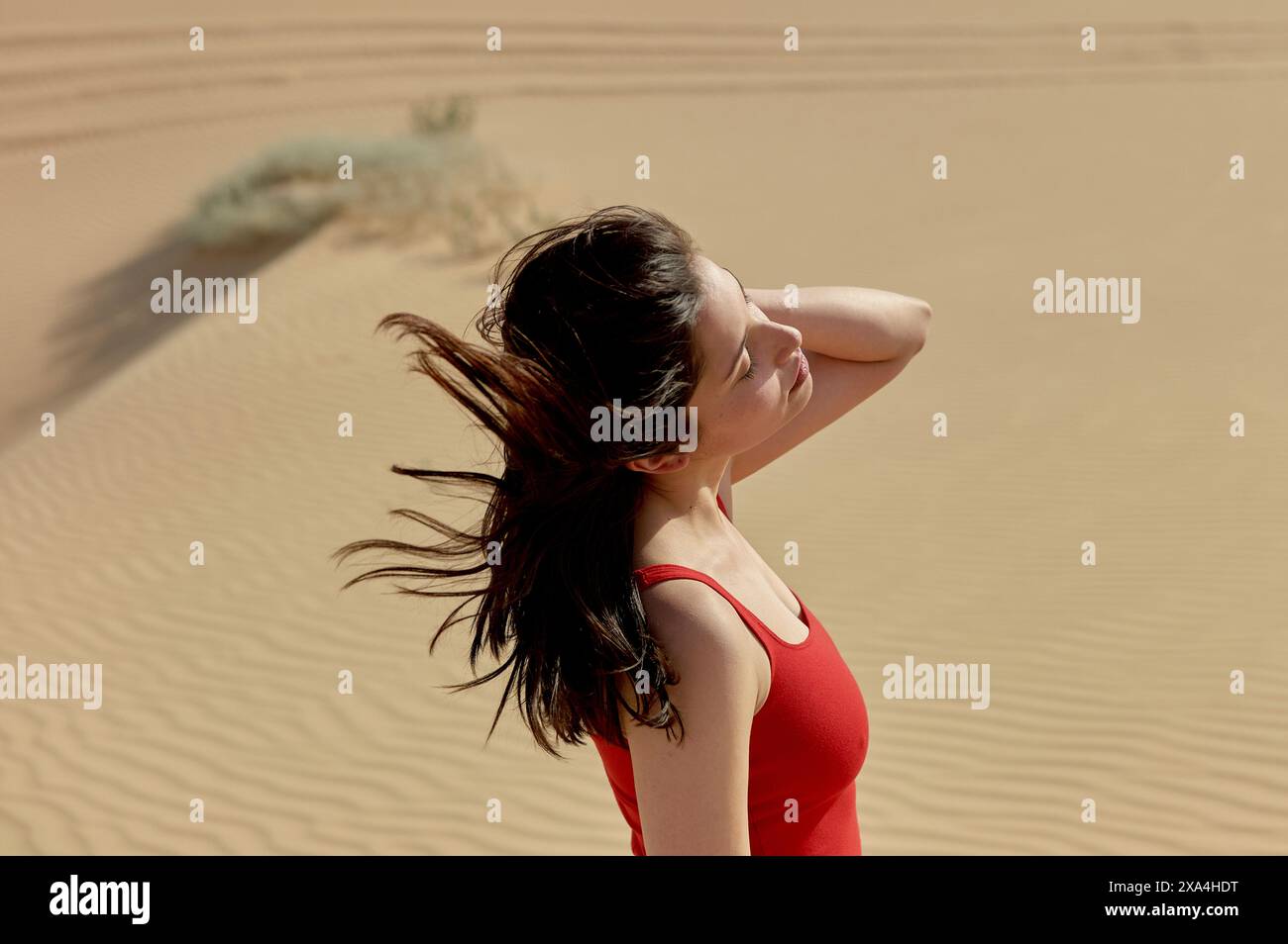 Eine Frau steht in einer Wüste, ihr Haar weht im Wind, während sie mit nachdenklichem Ausdruck in die Ferne blickt. Stockfoto