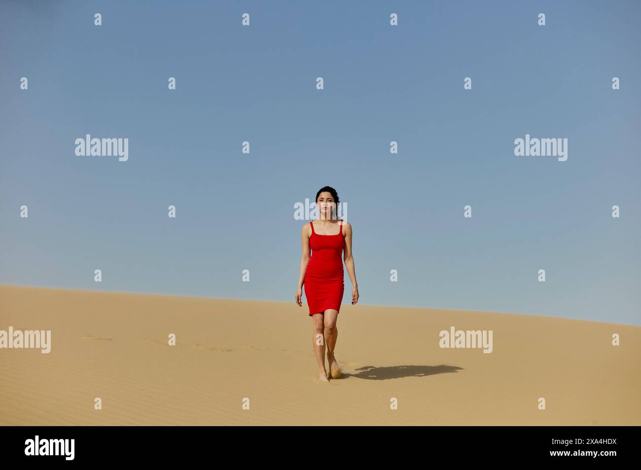 Eine Frau in rotem Kleid läuft allein auf einer Sanddüne unter klarem blauen Himmel. Stockfoto