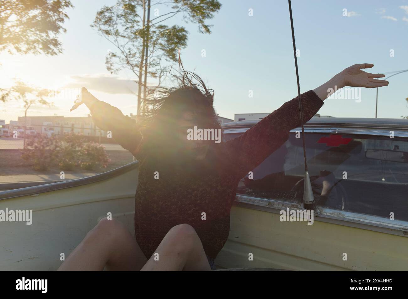 Eine freudige Person spreizt ihre Arme weit und nimmt den Wind mit ihren Haaren auf, während sie bei Sonnenuntergang in einem Boot fährt. Stockfoto