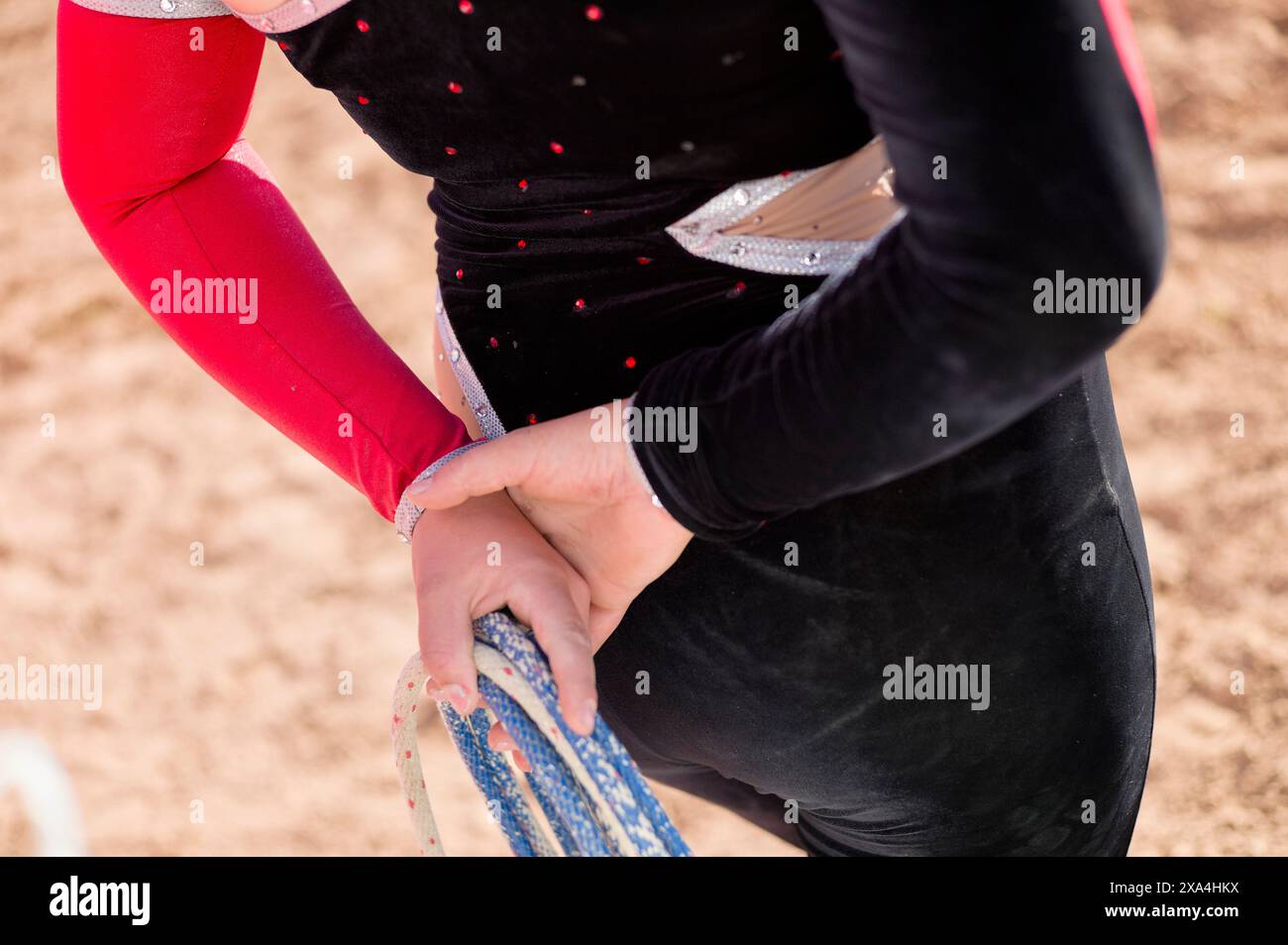 Eine Nahaufnahme einer Person in einem schwarz-roten Kostüm mit silbernen Akzenten, die ihre blau-silberne Eiskunstlauf-Klingenabdeckung anpassen. Stockfoto