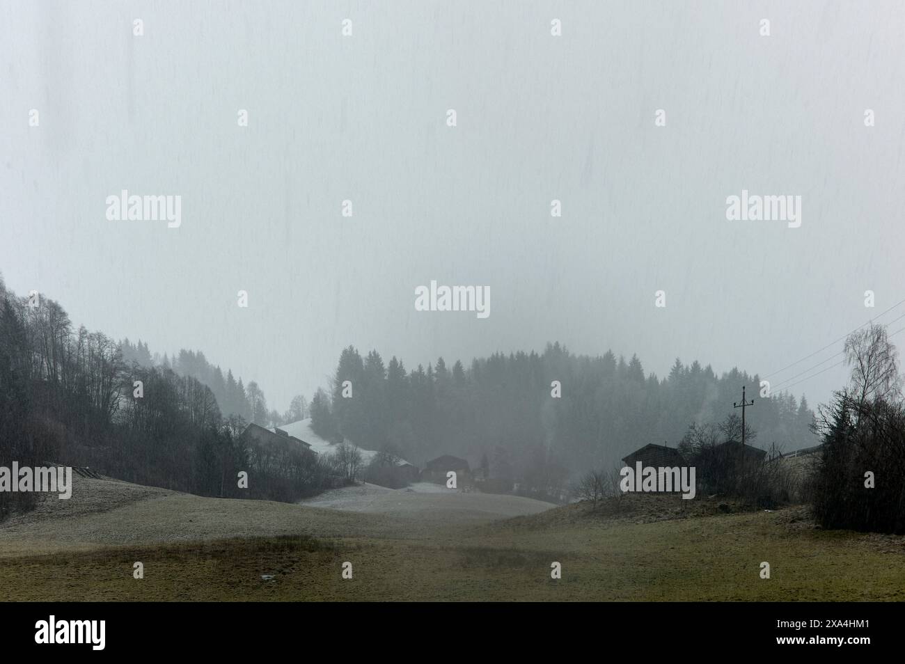 Eine nebelige Landschaftsszene mit schwachen Umrissen von Bäumen und Gebäuden in einer ländlichen Gegend bei Regenfällen. Stockfoto