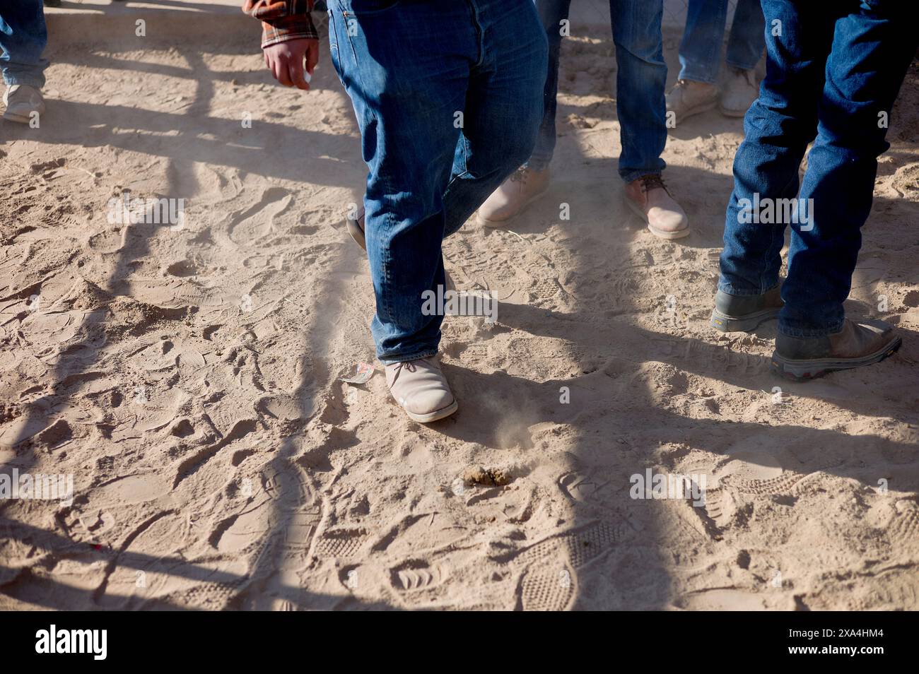 Eine Gruppe von Menschen, die auf sandigem Boden spazieren, fokussiert auf ihre unteren Körper und Schritte. Stockfoto