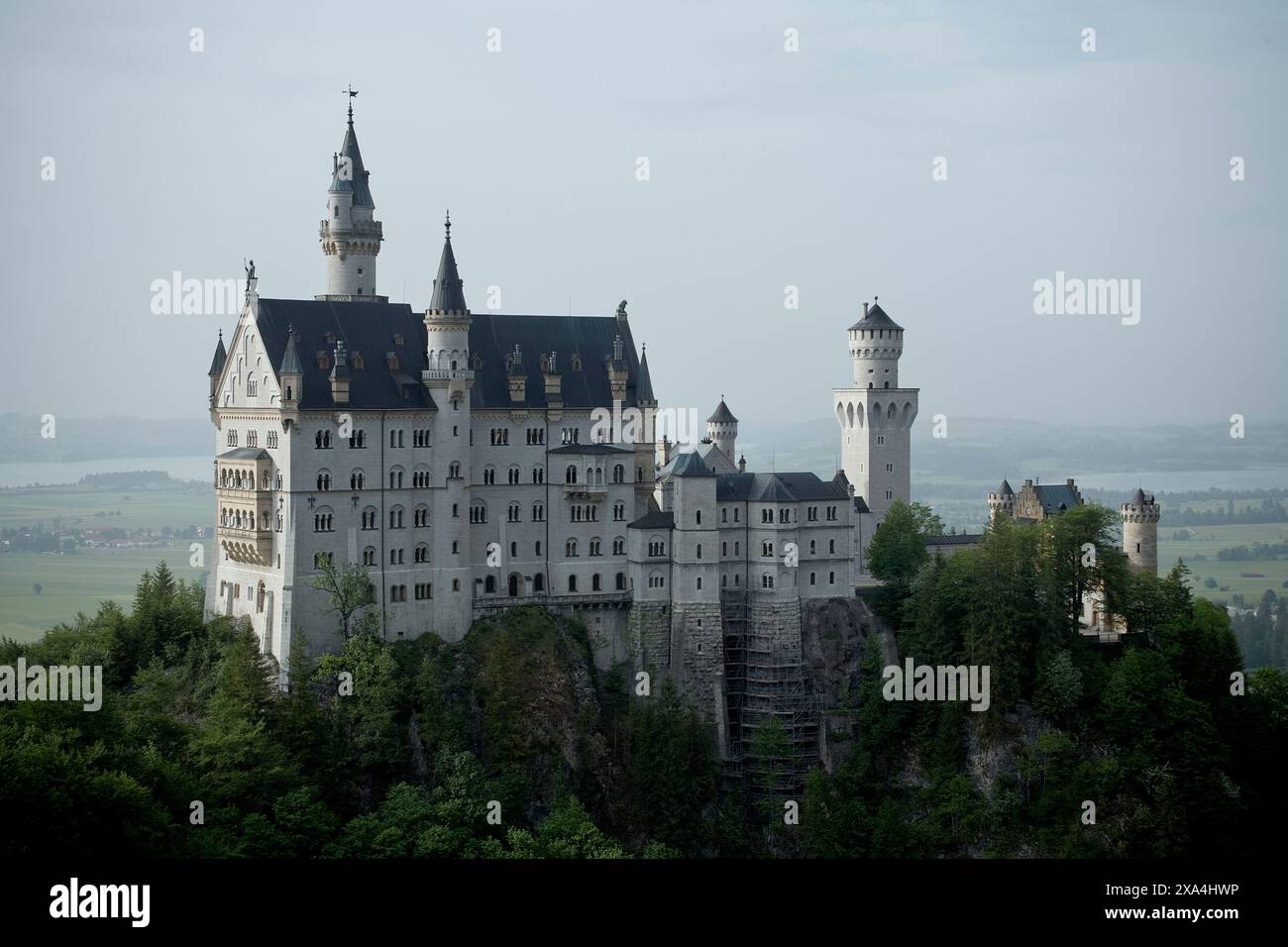 Majestätische Burg auf einem üppigen Hügel, umgeben von Grün und einem fernen See, unter einem trüben Himmel. Stockfoto