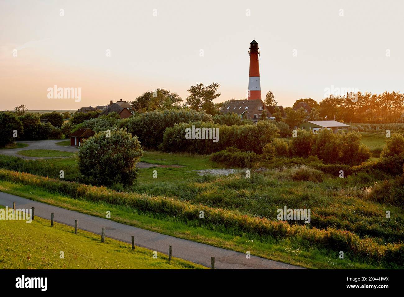 Ein ruhiger Sonnenuntergang umschließt einen malerischen Leuchtturm, der hoch zwischen üppigem Grün steht, mit einer kurvenreichen Straße, die in Richtung der ruhigen Szene führt. Stockfoto