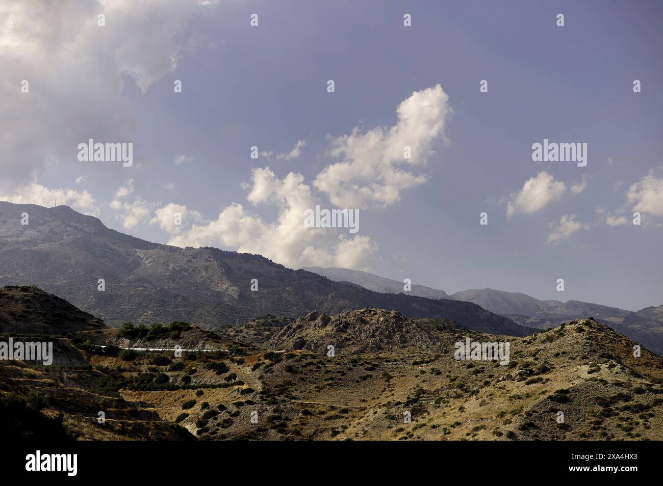 Wolken schweben über einer zerklüfteten Berglandschaft unter klarem Himmel. Stockfoto