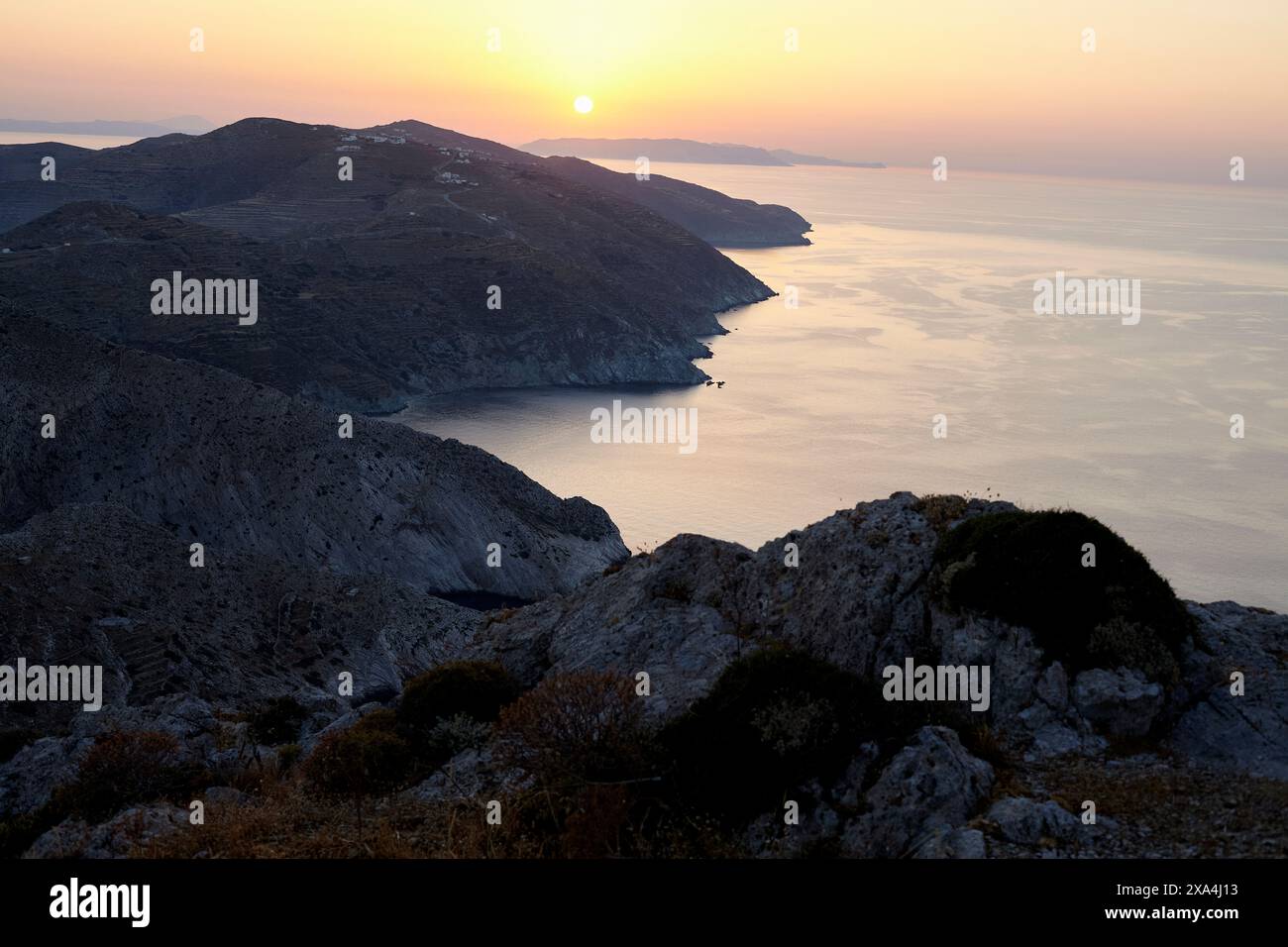 Ein ruhiger Sonnenuntergang über einer zerklüfteten Küste, während die Sonne ein warmes Licht über das Meer und felsiges Gelände wirft. Stockfoto