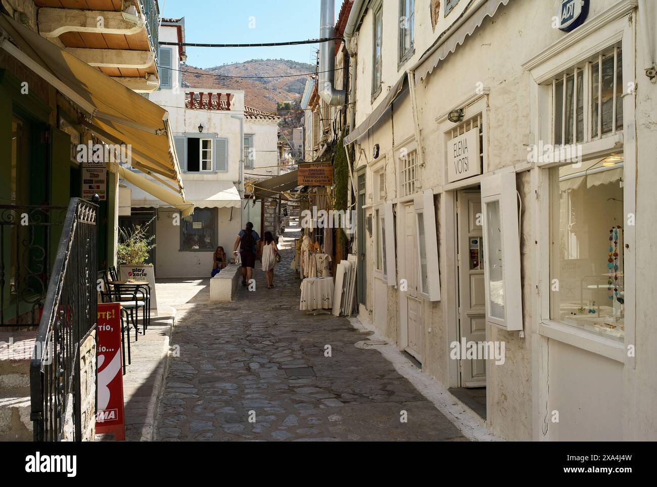 Ein sonniger Tag in einer engen Kopfsteinpflasterstraße, gesäumt von malerischen Gebäuden, Geschäften und Fußgängern in einer europäischen Stadt. Stockfoto