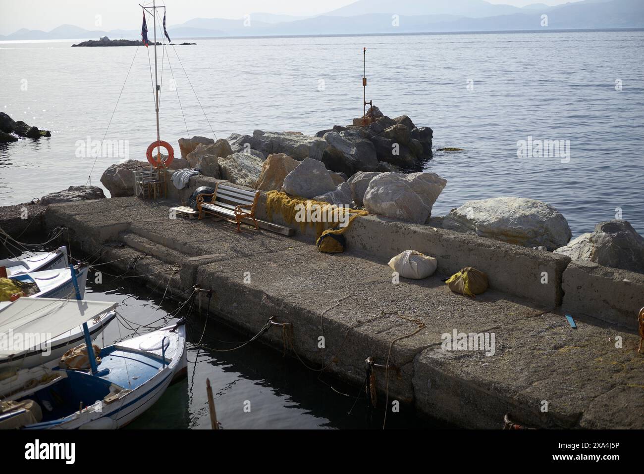 Eine ruhige Szene an einem Dock mit Booten, die neben einem Felsbrecher unter klarem Himmel vor Anker liegen. Stockfoto