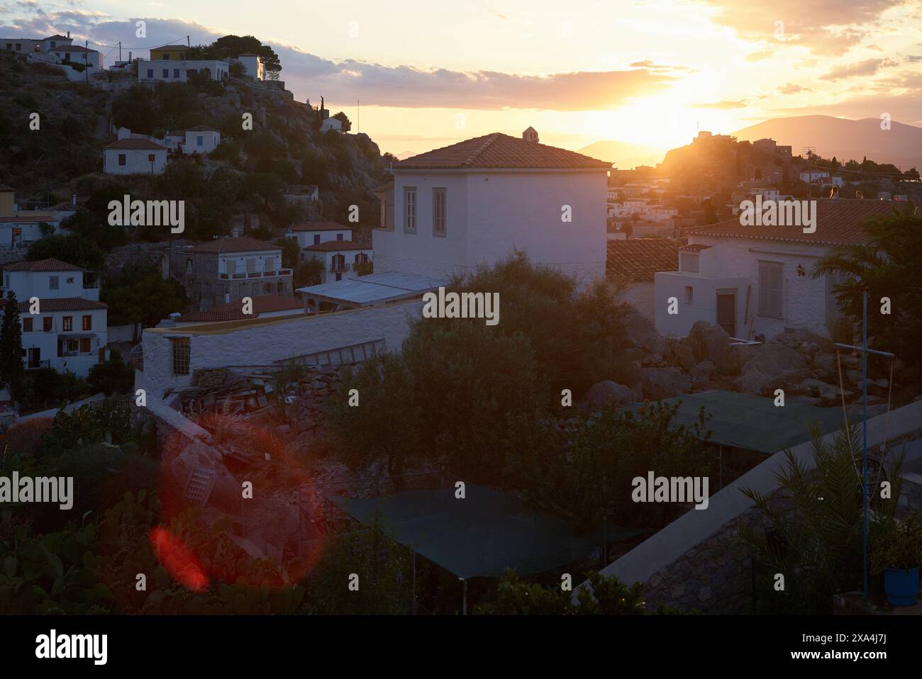 Blick auf den Sonnenuntergang über ein mediterranes Dorf mit sonnenverwöhnten Gebäuden und Vegetation im Vordergrund. Stockfoto