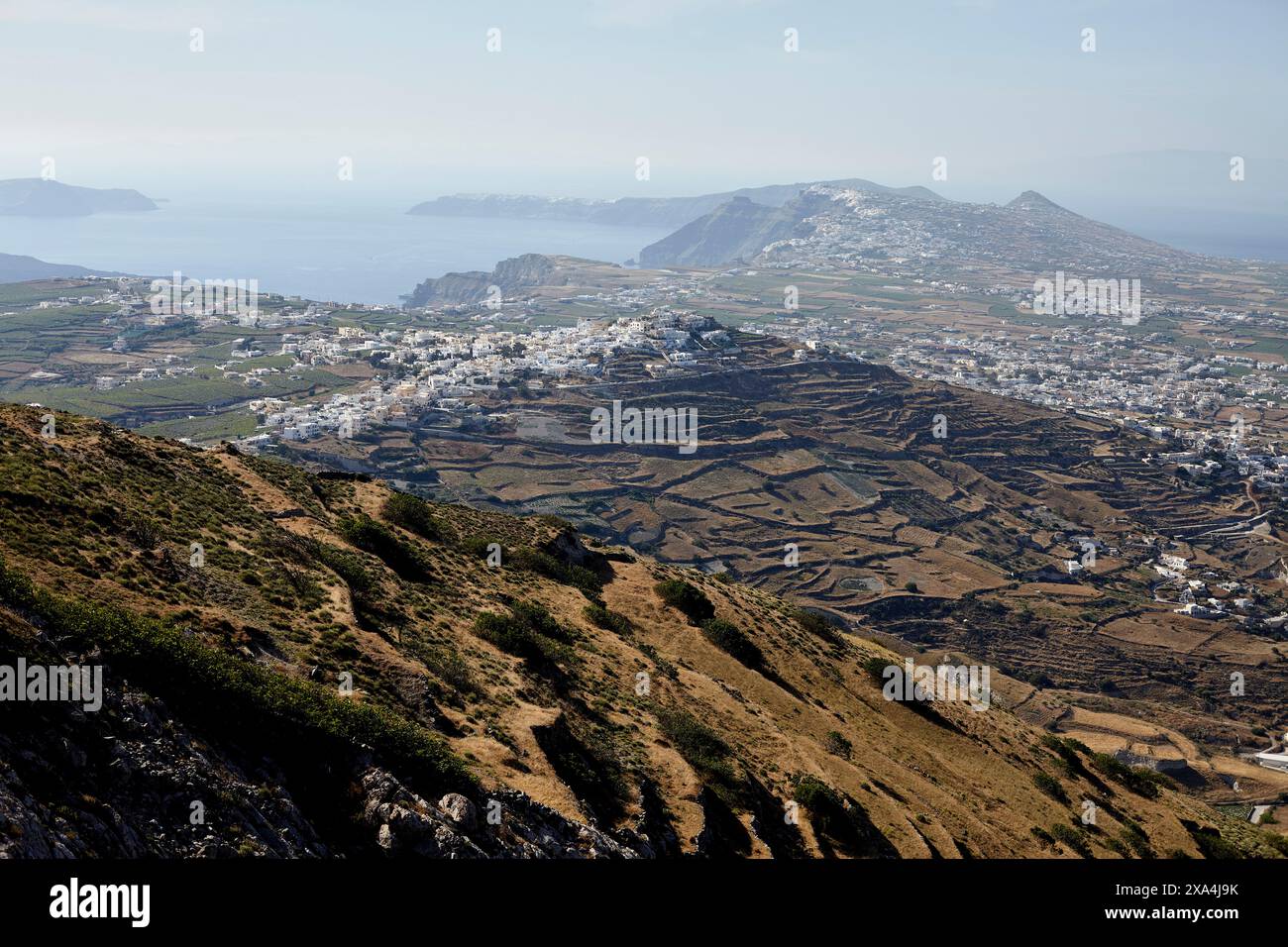 Ein atemberaubender Blick auf eine Küstenstadt mit weißen Gebäuden, eingebettet zwischen Terrassenhügeln, mit Blick auf das Meer mit Bergen in der Ferne. Stockfoto