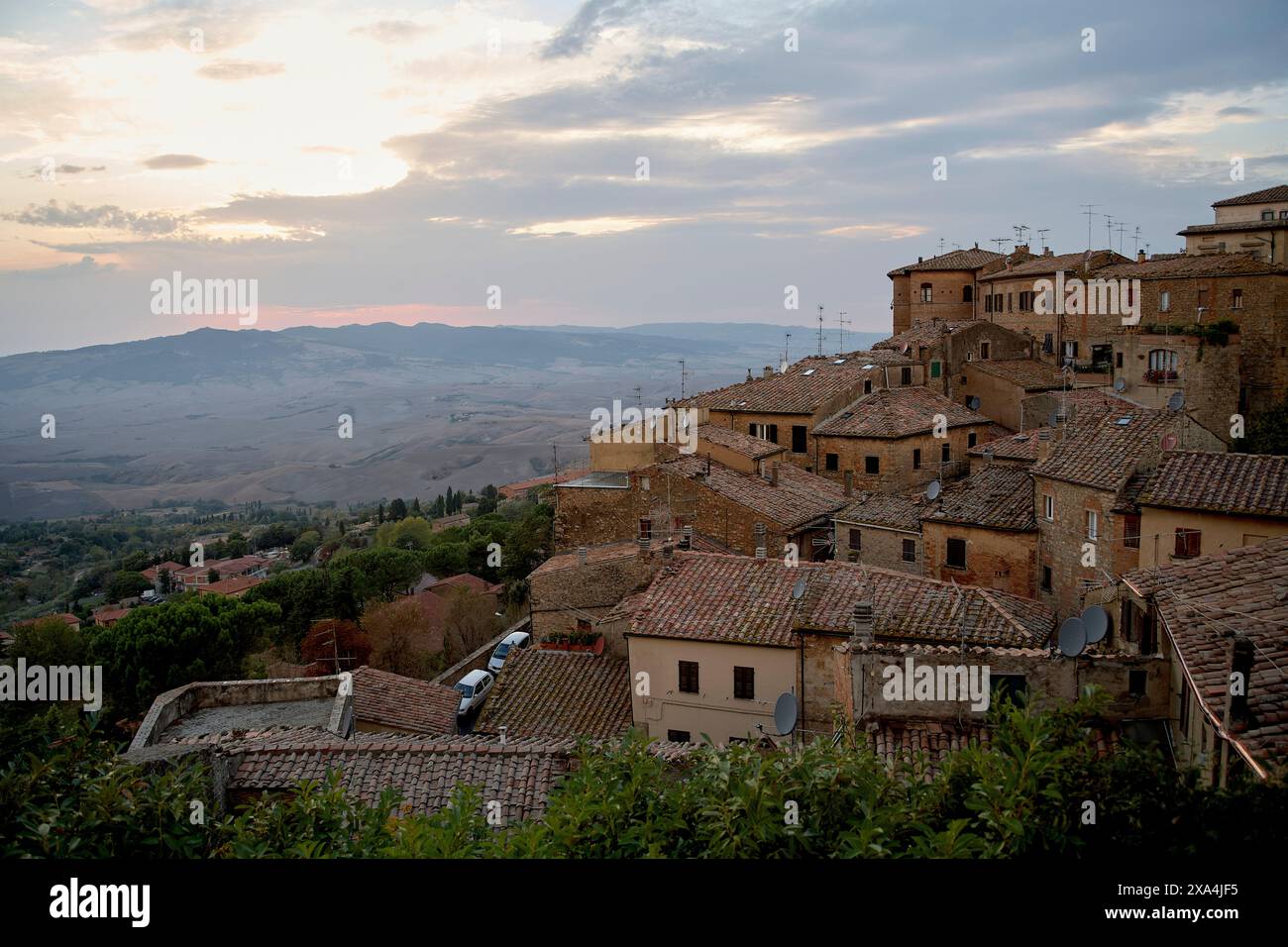 Blick auf den Sonnenuntergang über eine alte Stadt auf einem Hügel mit Terrakottadächern, umgeben von einer ländlichen Landschaft. Stockfoto