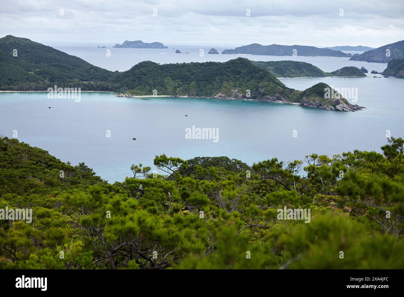 Ein malerischer Blick auf eine ruhige Bucht mit üppigem Grün im Vordergrund und mehreren kleinen Inseln in der Ferne unter einem bewölkten Himmel. Stockfoto