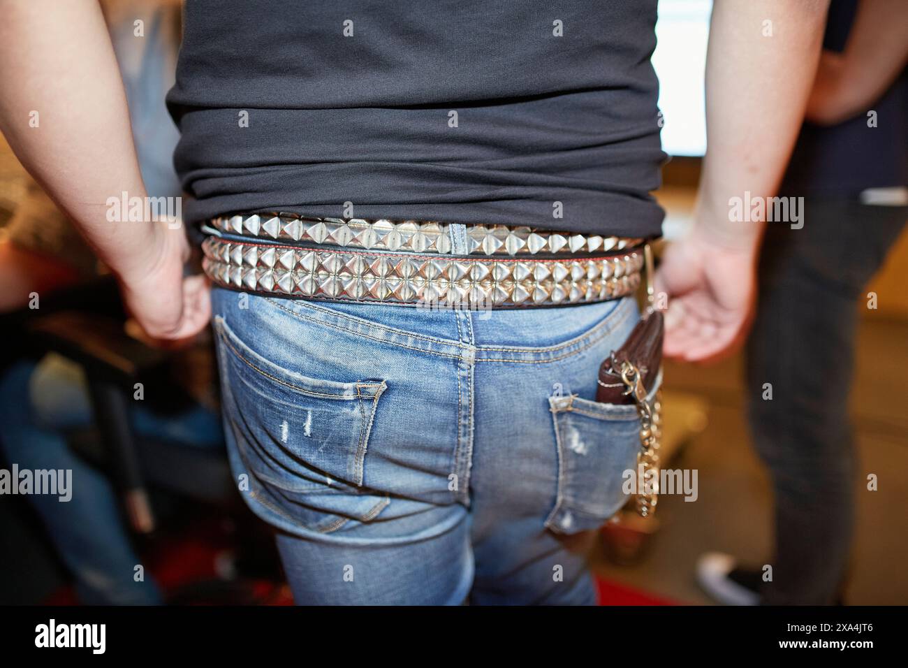 Nahaufnahme einer Person, die blaue Jeans und ein schwarzes Hemd trägt, mit Nietengürtel und Schlüsselanhänger, die an einer Gürtelschlaufe befestigt sind. Stockfoto